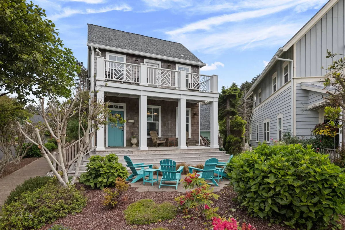 The front porch with a turquoise door and blue chairs surrounded by cheerful flower beds. This space is designed for relaxing, enjoying morning coffee, or hosting outdoor gatherings, with vibrant landscaping that adds to the inviting vibe.