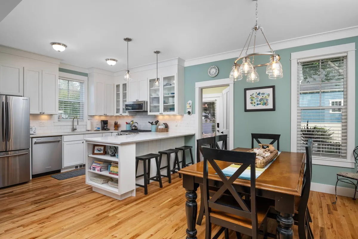 A close-up of the remodeled kitchen and dining table, featuring modern appliances, an island with bar stools, and ample natural light. The décor balances function and style, with inviting colors and a layout designed for conversation and shared meals.