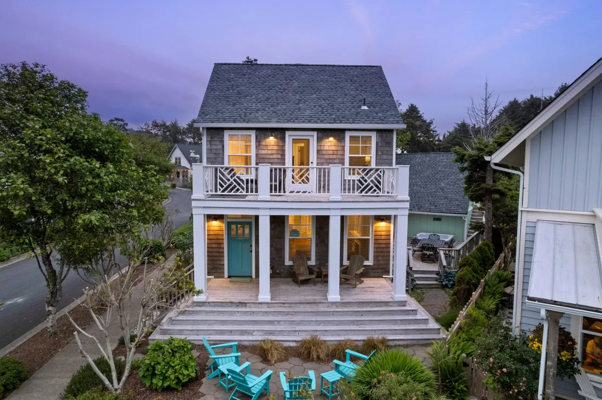 An inviting exterior view of the front porch, highlighted by a cheerful turquoise door and a pair of blue chairs. The porch is spacious and designed for relaxation and casual conversation, set against the backdrop of a glowing evening sky.