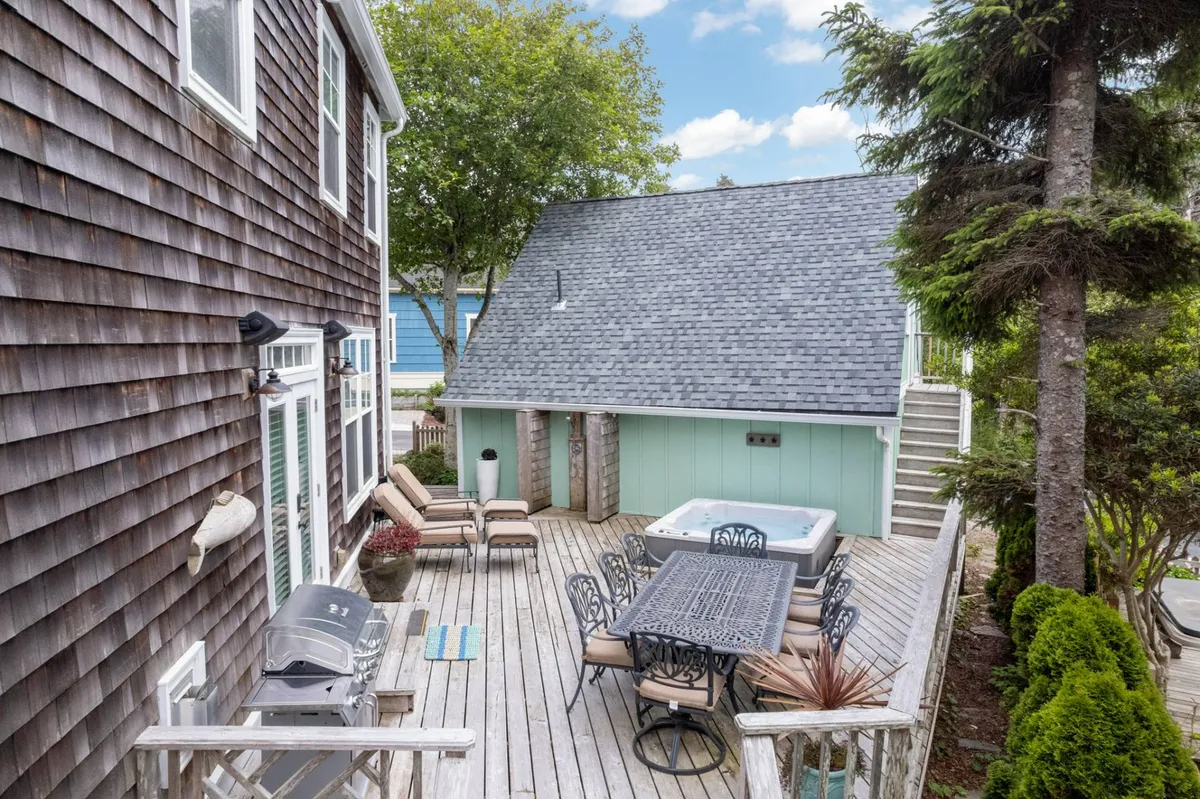 This image features a spacious wooden deck complemented by an outdoor dining set and a bubbling hot tub. The deck is surrounded by a landscaped garden, creating a private and relaxing outdoor retreat ideal for both dining and unwinding. Soft natural light highlights the seating and dining areas, and the garden adds a lush, tranquil ambiance.