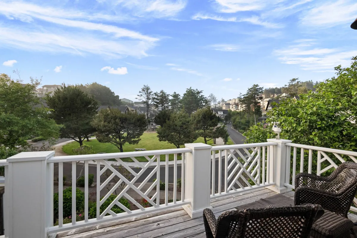 A peaceful balcony view overlooks a lush, green park with a visible seating area. The vantage point suggests a family-friendly neighborhood atmosphere, with the park setting ideal for watching children at play, relaxing outdoors, and soaking in nature. The scene conveys the accessibility of outdoor amenities within the Olivia Beach resort community.