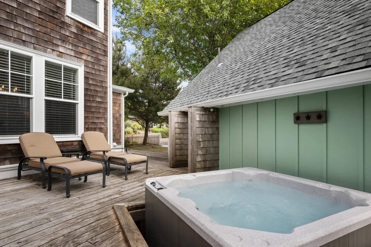 This image captures a serene exterior scene featuring a hot tub on a wooden deck, flanked by lounge chairs and a green privacy wall. The setting suggests a peaceful outdoor retreat perfect for relaxation, with an emphasis on connection to nature and the tranquility of the Olivia Beach community.