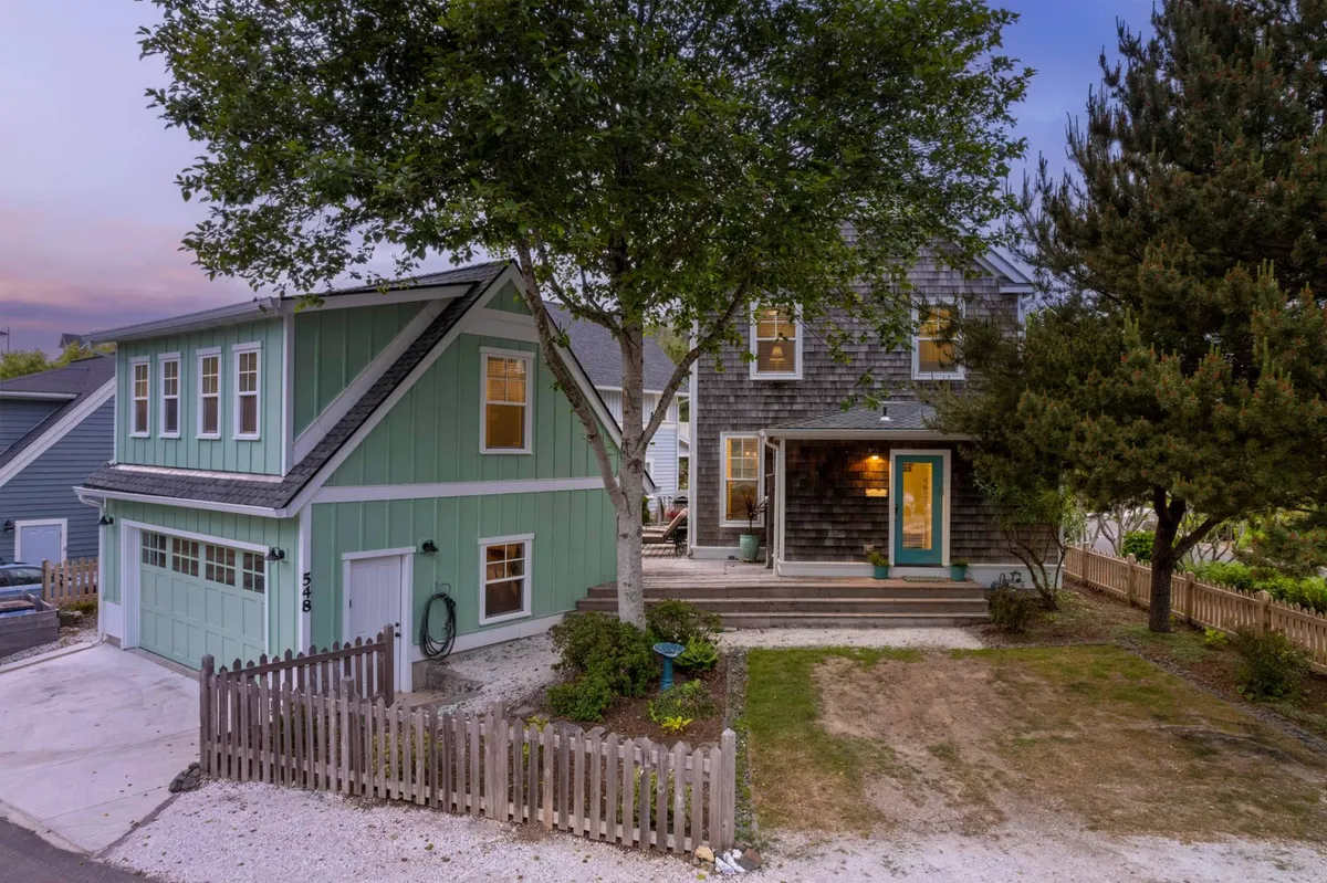 Two neighboring houses with wide porches and a large tree in the foreground. The area is set up for family gatherings, outdoor dining, or evening strolls, reinforcing the sense of a close-knit, vibrant community setting.