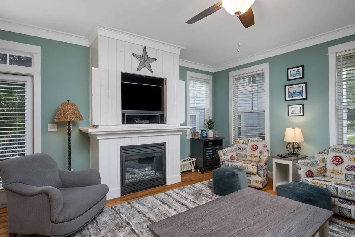 A cozy living area centered around a fireplace, with comfortable seating, a decorative star, and art on the walls. The natural light, plush furnishings, and coastal-inspired décor create a relaxing space for unwinding after a day at the beach.