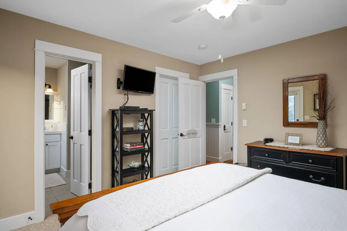 A calm, spacious bedroom featuring a bed, dresser, shelf, mirrors, and doors. The soothing atmosphere suggests privacy and relaxation, making it suitable for a secluded guest suite or carriage house room.