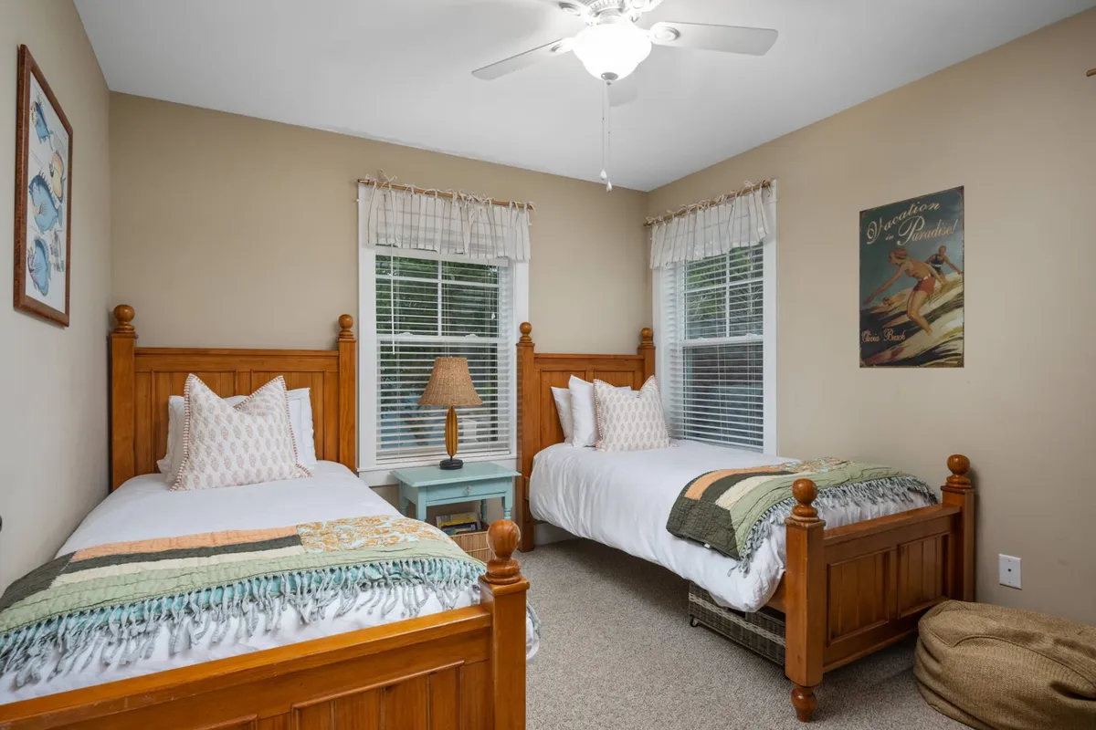 A welcoming bedroom with two twin beds, a lamp on the nightstand, decorative artwork on the wall, and textured throw blankets. The scene conveys comfort and warmth, perfect for family members or friends sharing the space.