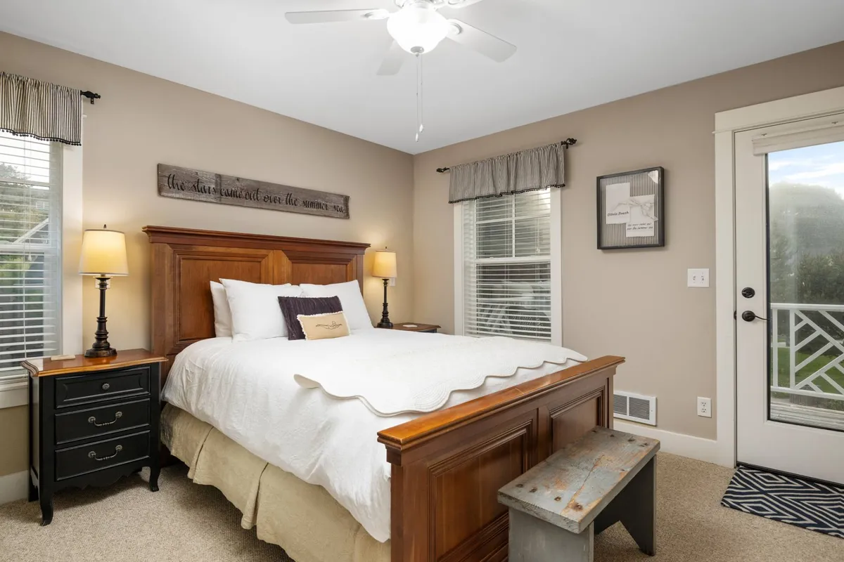 A warm and relaxing bedroom with a wooden bed frame, nightstands with lamps, decorative wall art, and a door leading to an outdoor space. Sunlight filters in, creating a cozy and inviting atmosphere ideal for restful nights and gentle mornings.