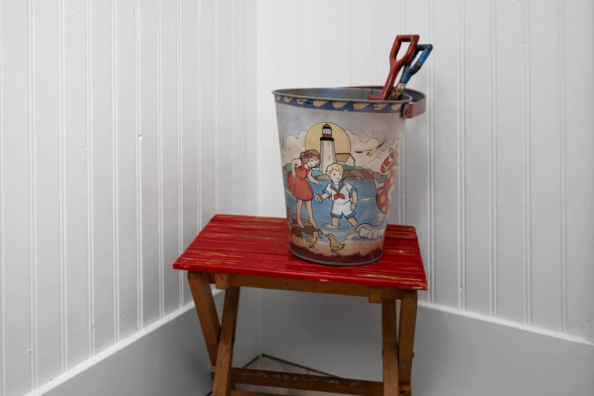 A playful, whimsical interior scene featuring a colorful children's bucket with illustrated motifs and a red stool, evoking a lighthearted, family-focused atmosphere. The image hints at activities for children and family bonding moments, connecting with the mention of the playground and child-friendly amenities.